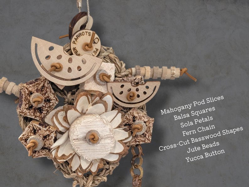 May include: A bird toy featuring mahogany pod slices, balsa squares, sola petals, a fern chain, cross-cut basswood shapes, jute beads, and a yucca button. The text lists these materials: Mahogany Pod Slices, Balsa Squares, Sola Petals, Fern Chain, Cross-Cut Basswood Shapes, Jute Beads, Yucca Button.