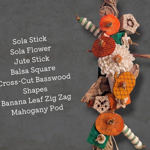 May include: A bird toy featuring a vertical arrangement of colorful components including a sola stick, sola flower, jute stick, balsa square, cross-cut basswood shapes, banana leaf zig zag, and a mahogany pod, with the text listing these materials.
