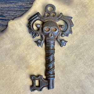 Puede incluir: Una llave decorativa de estilo antiguo hecha de metal marrón oscuro. La llave presenta un diseño de calavera en la parte superior, con detalles ornamentados y un mango retorcido. La llave es probablemente para fines decorativos.