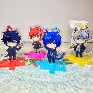 Op de afbeelding: Acryl sleutelhangers met anime-stijl personages met kattenoren. Elk personage is gekleed in een unieke outfit en staat op een kleurrijke puzzelstuk basis. De sleutelhangers hebben een heldere, glanzende afwerking en zijn bevestigd aan een metalen sleutelhanger.