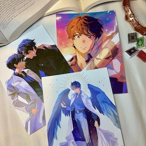 Può includere: Una collezione di stampe artistiche in stile anime con personaggi maschili. Le stampe presentano varie pose e stili, con colori vivaci e illustrazioni dettagliate. Una stampa raffigura un personaggio con ali blu e un'aureola.