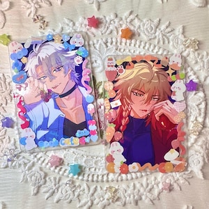 May include: Two clear acrylic charms featuring anime-style male characters with white and blonde hair, framed by colorful, decorative borders with bunny and star accents. The charms are embellished with small, iridescent stickers.