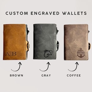 May include: Three custom engraved wallets in brown, grey, and coffee colours. The brown wallet has the initials "AB", the grey wallet has a dragon graphic with the name "ALEX", and the coffee wallet has an anchor graphic with the name "BRYTEN".