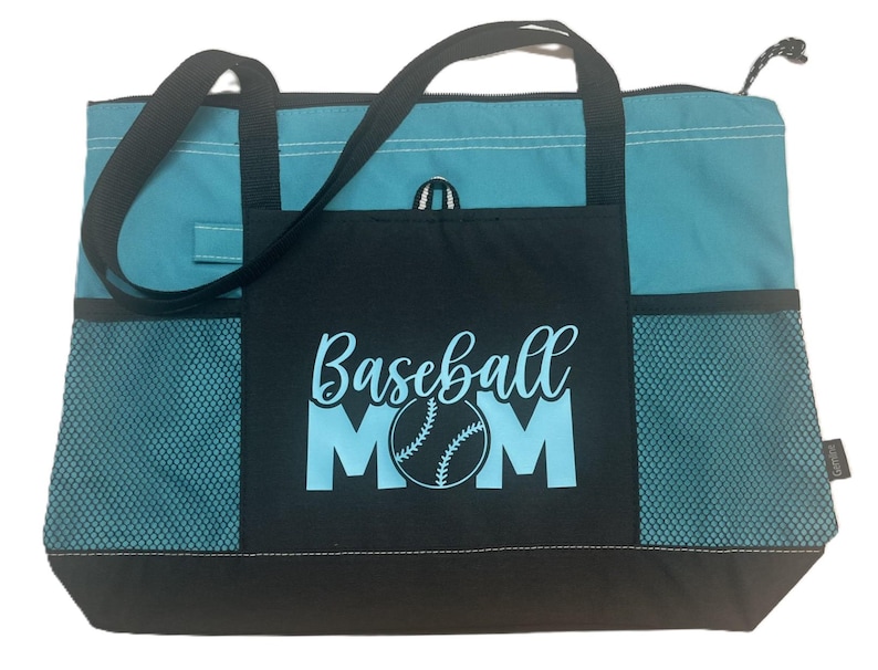 K&ouml;nnte beinhalten: Eine t&uuml;rkisfarbene und schwarze Tragetasche mit einem Netzfach auf jeder Seite. Das vordere Fach hat den Text "Baseball Mom" in hellblau mit einer Baseballgrafik.