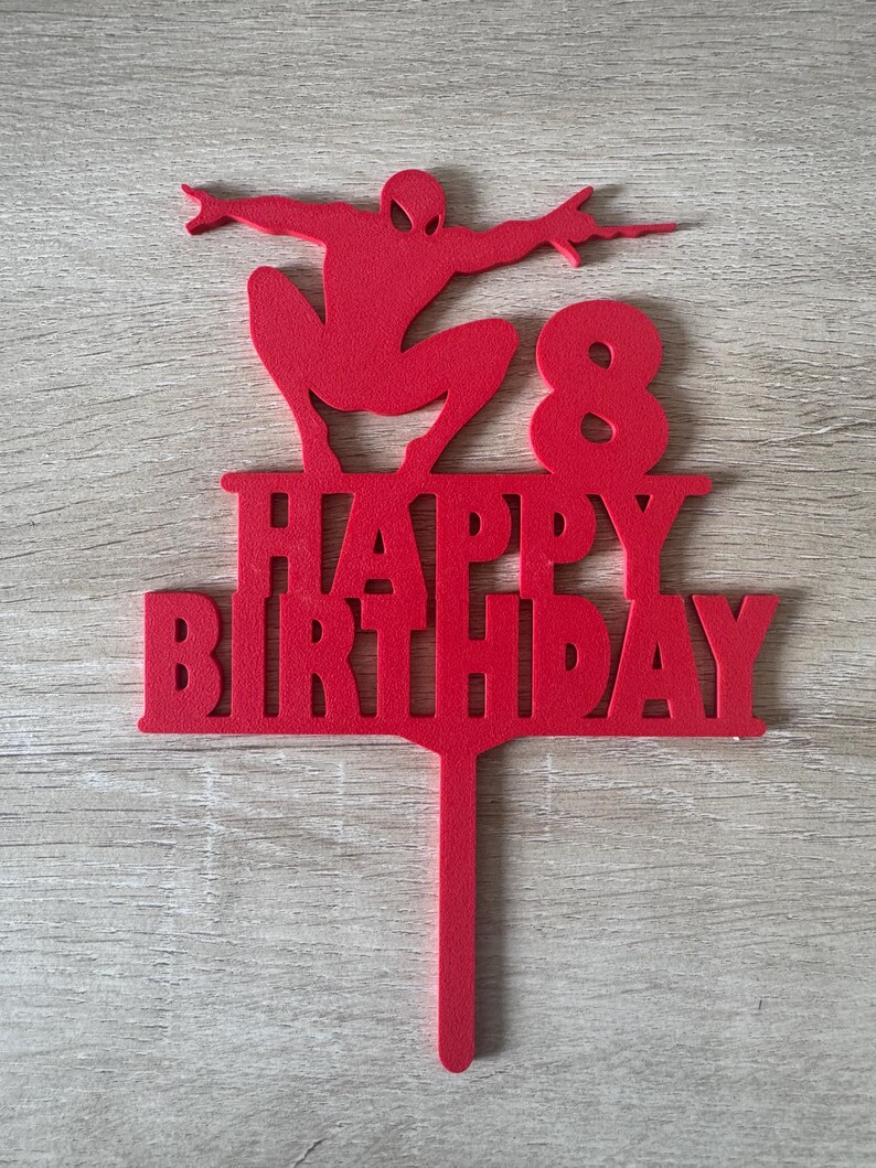 Puede incluir: Un adorno rojo para pastel con la silueta de un superh&eacute;roe, las palabras "HAPPY BIRTHAY" y el n&uacute;mero "8". Este adorno est&aacute; dise&ntilde;ado para una celebraci&oacute;n de cumplea&ntilde;os.