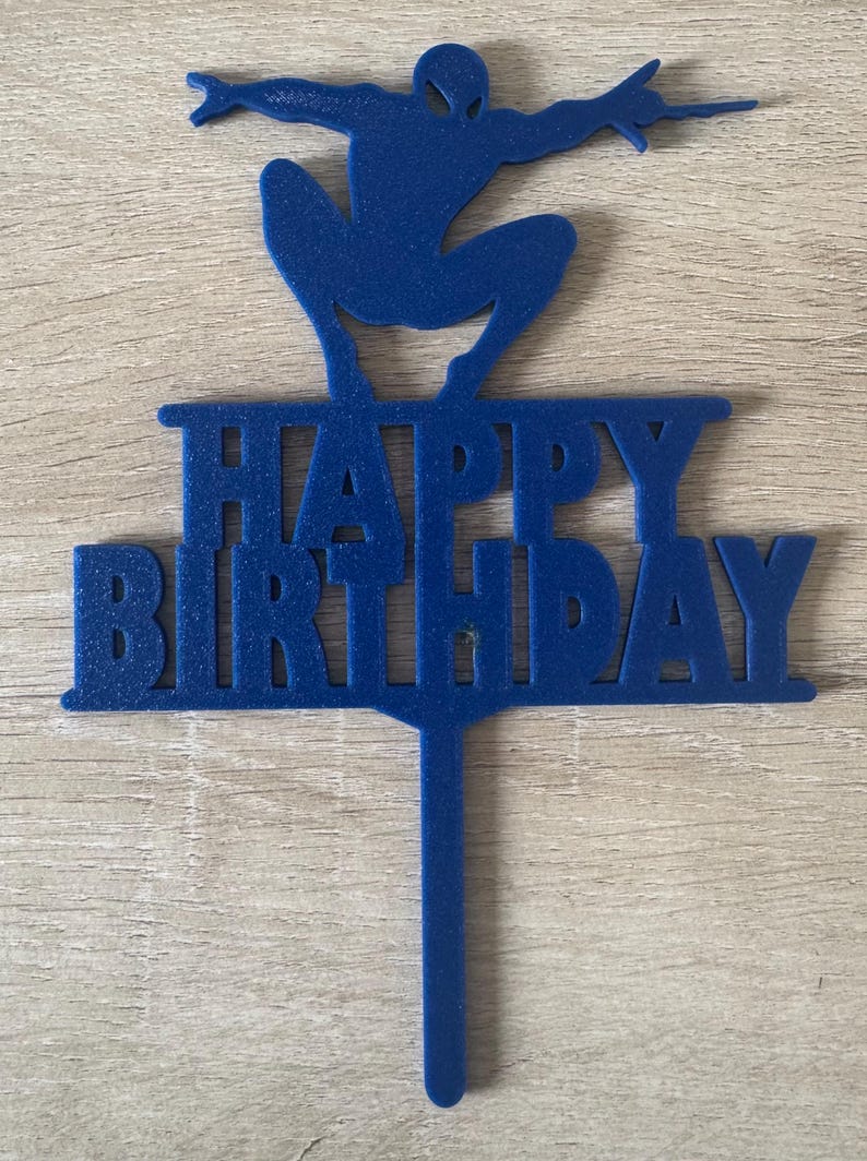 Puede incluir: Adorno azul para tarta con la silueta de un superh&eacute;roe y la inscripci&oacute;n "HAPPY BIRTHDAY". El adorno es de material s&oacute;lido y tiene un pin para insertar en una tarta.