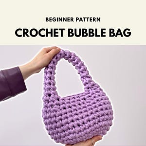 May include: A light purple crochet bubble bag with a rounded shape and a single integrated handle. The text at the top reads BEGINNER PATTERN CROCHET BUBBLE BAG. The bag is constructed from thick yarn with a visible, textured, knotted stitch pattern.