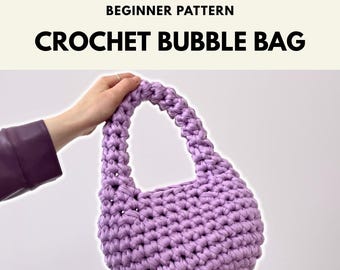May include: A light purple crochet bubble bag with a rounded shape and a single integrated handle. The text at the top reads BEGINNER PATTERN CROCHET BUBBLE BAG. The bag is constructed from thick yarn with a visible, textured, knotted stitch pattern.