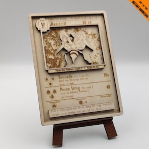 Puede incluir: Una carta de juego de Pokemon de madera con Beedrill, un Pokemon Abeja Veneno. La carta tiene un fondo marrón con una imagen de Beedrill en el centro. La carta tiene texto que describe las habilidades y estadísticas de Beedrill. La carta está en un pequeño caballete de madera.