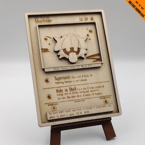 May include: A wooden Pokemon card featuring Shellder, a Bivalve Pokemon. The card has a brown background with a light brown border. The card features a picture of Shellder in the upper right corner. The card has the text "Shellder" in large, bold letters at the top. The card also has the text "30 HP" in the upper right corner. The card has the text "Supersonic Flip a coin. If heads, the Defending Pokemon is now Confused." in the middle left. The card has the text "Hide in Shell Flip a coin. If heads, prevent all damage done to Shellder during your opponent's next turn. (Any other effects of attack still happen.)" in the middle left. The card has the text "Its hard shell repels any kind of attack. It vulnerable only when its shell is open. LV. 8 #90" in the bottom left.