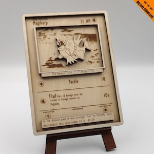 May include: A wooden Pokemon card featuring Magikarp, a fish Pokemon. The card has a brown background with white text and a picture of Magikarp in the center. The card is on a wooden easel. The text on the card reads "Magikarp", "30 HP", "Fish Pokemon", "Tackle", "Flail", "Weakness", "Resistance", "Retreat Cost", "In the distant past, it was stronger than its horribly weak descendants that exist today. LV. 8 #129".