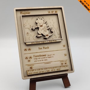 May include: A wooden Pokemon card featuring Magmar, a Spitfire Pokemon. The card has a brown background with a white border. The card has a picture of Magmar in the upper left corner. The card has the text "Magmar" in the upper left corner, "50 HP" in the upper right corner, "Spitfire Pokemon. Length: 4' 3", Weight: 98 lbs." in the middle left, "Fire Punch" in the middle left, "30" in the middle right, "Flamethrower" in the bottom left, "Discard 1 Energy card attached to Magmar in order to use this attack" in the bottom left, "50" in the bottom right, "weakness" in the bottom left, "resistance" in the bottom middle, "retreat cost" in the bottom right, and "If it fails to crush the victim in its pincers, it will swing its victim around and toss it hard.. LV. 24 #127" in the bottom center.