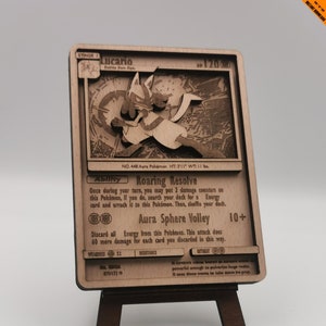 May include: A wooden Pokemon card featuring Lucario, a fighting-type Pokemon. The card is brown and features a detailed illustration of Lucario in a fighting pose. The card's text reads "Lucario, Aura Pokemon, No. 448, HT: 3'11", WT: 11 lbs.  The card also features the text "Roaring Resolve" and "Aura Sphere Volley".