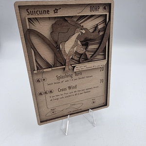 Könnte beinhalten: Hölzerne Suicune Pokémon-Karte mit detailliertem Laserschnitt-Design. Die Karte zeigt den Namen des Charakters, HP und Angriffsdetails. Die Karte wird auf einem transparenten Acryl-Ständer präsentiert.