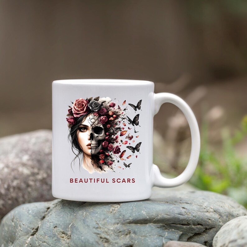 May include: White ceramic mug featuring a striking design of a woman's face transitioning into a skull, adorned with roses and butterflies. The mug has the text "BEAUTIFUL SCARS" in a dark red font.