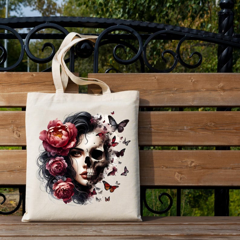 May include: A beige tote bag featuring a striking design of a woman's face, half human and half skull, adorned with burgundy flowers and butterflies. The bag has a simple, practical design with two handles.