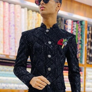 K&ouml;nnte beinhalten: Ein schwarzer Blazer mit einem Paillettenmuster und einem Stehkragen. Der Blazer hat einen einzigen Knopfverschluss und eine Tasche auf der linken Seite. Das Model tr&auml;gt eine schwarze Hose und schwarze Schuhe.