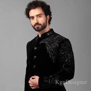 May include: A black velvet suit jacket with a black embroidered design on the right shoulder. The jacket has a mandarin collar and a button closure.