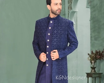 Puede incluir: Una chaqueta larga azul con estampado, con una kurta y pantalones azules a juego. El atuendo está adornado con botones plateados y un ribete plateado. El modelo lleva zapatos azules a juego.