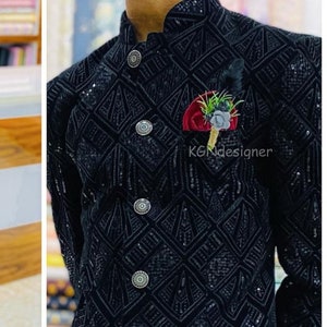 K&ouml;nnte beinhalten: Ein schwarzer Samtblazer mit geometrischem Muster und silbernen Kn&ouml;pfen. Der Blazer hat einen Stehkragen und ein Einstecktuch mit einer roten Blume und gr&uuml;nen Bl&auml;ttern.