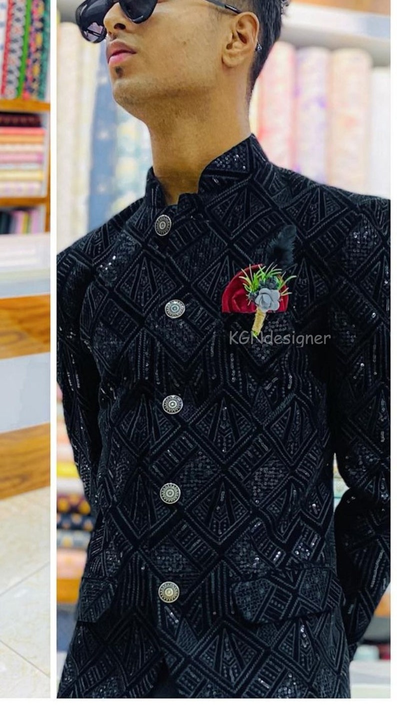 K&ouml;nnte beinhalten: Ein schwarzer Samtblazer mit geometrischem Muster und silbernen Kn&ouml;pfen. Der Blazer hat einen Stehkragen und ein Einstecktuch mit einer roten Blume und gr&uuml;nen Bl&auml;ttern.