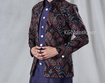 May include: A man wearing a navy blue patterned jacket over a blue shirt and matching pants. The jacket has a mandarin collar and is decorated with a colorful geometric design. The man is standing against a light gray background.