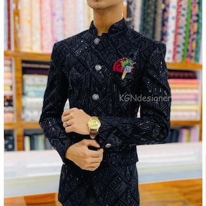 K&ouml;nnte beinhalten: Ein schwarzer Samtblazer mit geometrischem Muster und Pailletten. Der Blazer hat einen Stehkragen und einen einzigen Knopfverschluss. Der Blazer wird von einer Person mit einer Uhr am Handgelenk getragen.