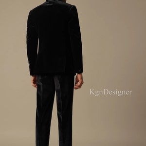 May include: A black velvet suit jacket and matching pants. The jacket has a mandarin collar and the suit is worn by a person standing with their back to the camera.