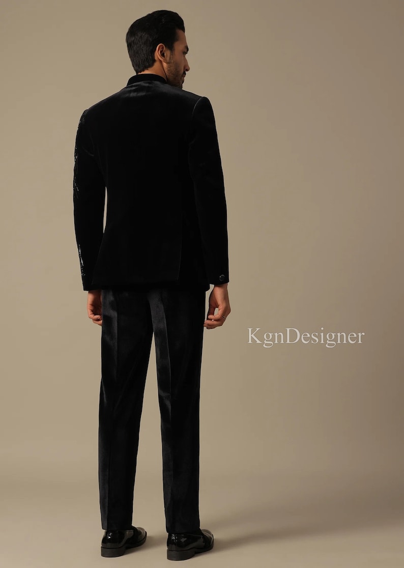 May include: A black velvet suit jacket and matching pants. The jacket has a mandarin collar and the suit is worn by a person standing with their back to the camera.