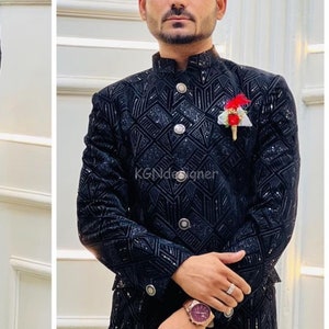 K&ouml;nnte beinhalten: Ein schwarzer Samtblazer mit geometrischem Muster und silbernen Kn&ouml;pfen. Der Blazer hat einen Stehkragen und eine kleine rote Blumennadel am Revers. Der Text "KGNDesigner" ist auf dem Blazer sichtbar.