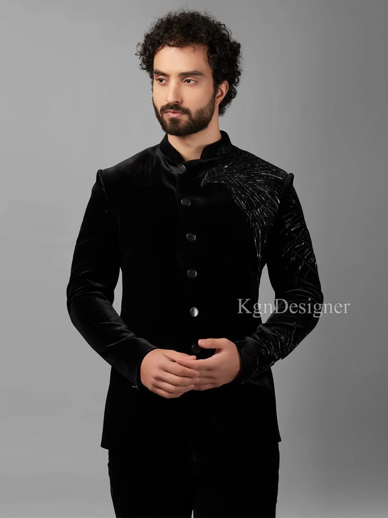 May include: A black velvet blazer with a mandarin collar and a single button closure. The blazer features a black embroidered design on the right shoulder.