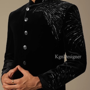 May include: A black velvet men's kurta with silver embroidery. The kurta has a mandarin collar and a button closure. The embroidery is in the shape of a bird's wing.