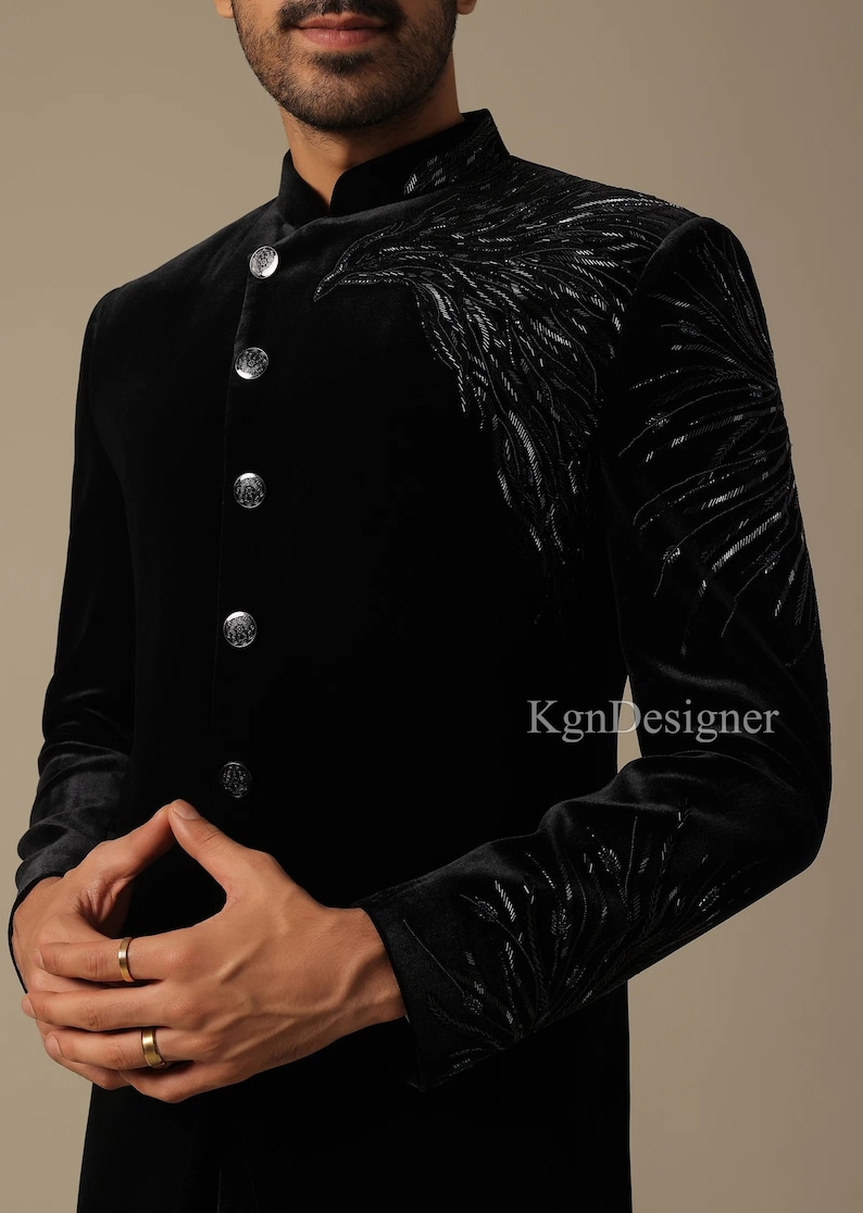 May include: A black velvet men's kurta with silver embroidery. The kurta has a mandarin collar and a button closure. The embroidery is in the shape of a bird's wing.