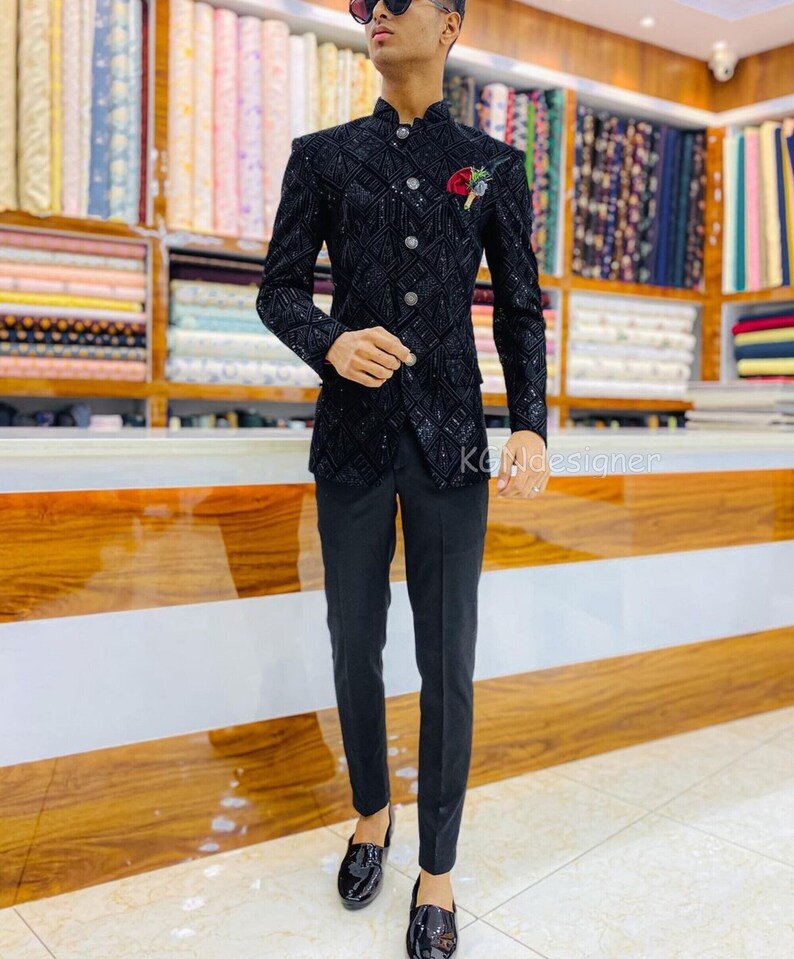 K&ouml;nnte beinhalten: Ein schwarzer Blazer mit einem Paillettenmuster und einem Stehkragen. Der Blazer hat einen einzigen Knopfverschluss und eine Tasche auf der linken Seite. Das Model tr&auml;gt eine schwarze Hose und schwarze Schuhe.