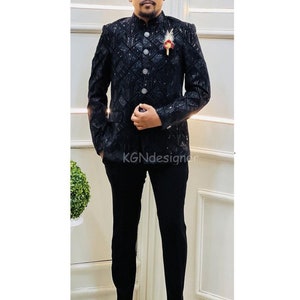 K&ouml;nnte beinhalten: Ein schwarzer Blazer mit einem Paillettenmuster und einem Stehkragen. Der Blazer hat einen Knopfverschluss und wird &uuml;ber einer schwarzen Hose getragen.