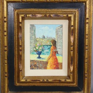 May include: A framed oil painting depicting a woman in a red dress standing in a window overlooking a cityscape. The woman is looking out the window at the city, which is painted in a bright, colorful style. There is a vase of flowers on the windowsill.