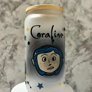 Pu&ograve; includere: Un barattolo di vetro bianco con un coperchio in bamb&ugrave;, con un design dipinto a mano di Coraline dal film Coraline. Il design include una spirale in bianco e nero, stelle e un bottone.