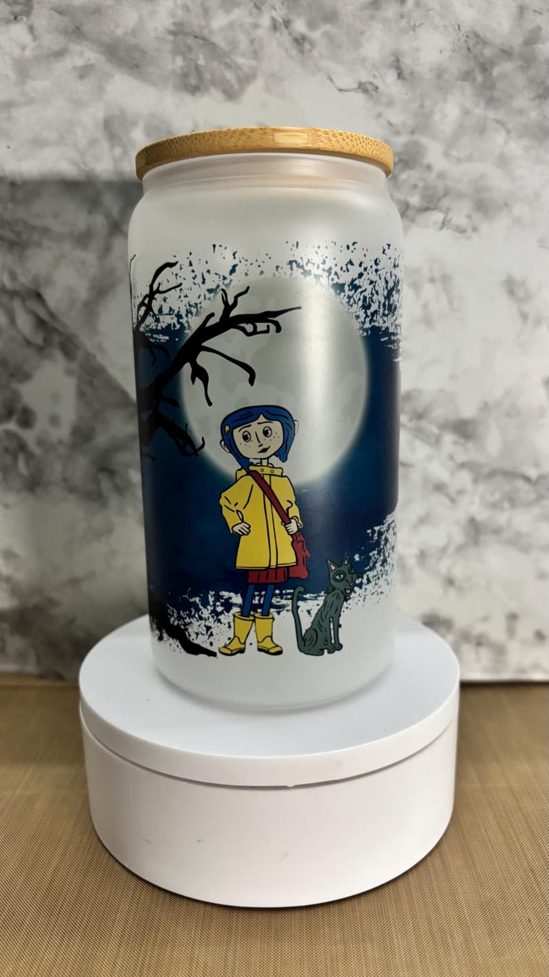Pu&ograve; includere: Un barattolo di vetro smerigliato con un coperchio in bamb&ugrave; che presenta un'illustrazione di cartone animato di una ragazza con un impermeabile giallo e un gatto nero in piedi di fronte a una luna piena. Lo sfondo &egrave; blu scuro con schizzi di vernice bianca.