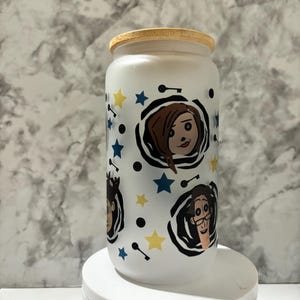 Pu&ograve; includere: Un barattolo di vetro bianco smerigliato con un coperchio di legno. Il barattolo ha un design colorato con personaggi dei cartoni animati con vortici in bianco e nero, stelle gialle e stelle blu.