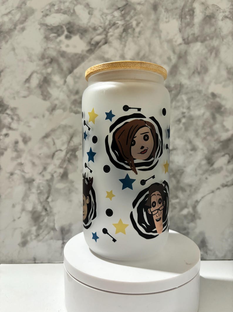 Pu&ograve; includere: Un barattolo di vetro bianco smerigliato con un coperchio di legno. Il barattolo ha un design colorato con personaggi dei cartoni animati con vortici in bianco e nero, stelle gialle e stelle blu.