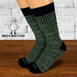 Peut inclure: Chaussettes noires avec un motif de code binaire vert. Les chaussettes ont le texte "SOCKSico" sur le bas.