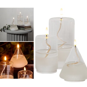 Könnte beinhalten: Ein Satz mit drei gläsernen Öllampen mit weißem Wachs und Dochten. Die Lampen haben verschiedene Formen, darunter einen Zylinder, einen Kegel und eine Pyramide. Die Lampen sind angezündet und die Flammen sind sichtbar.