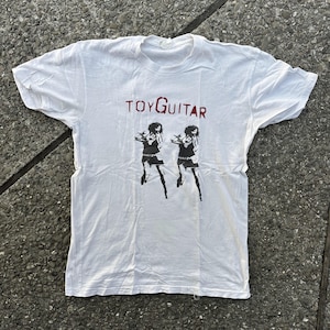 May include: White t-shirt with a red "TOYGUITAR" text and a black and white image of two women in short skirts and boots.