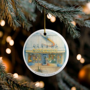 May include: A round Christmas ornament with a watercolor illustration of a shop called "World of Mirth" in Richmond, Virginia. The shop has a yellow awning and a rocket ship graphic. The ornament hangs from a gold string.