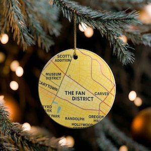 May include: A round, yellow Christmas ornament with a map of a city district. The map includes street names and district labels such as "The Fan District" and "Carytown". The ornament hangs from a gold string.