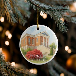 May include: Round ceramic Christmas ornament featuring a watercolor painting of Ferrum College's main building. The building is red brick with white columns and a blue roof. The ornament hangs from a gold string.
