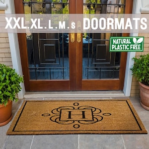 May include: A brown coir doormat with a black border and a monogram of the letter "H" in a decorative frame. The doormat is labeled "Natural Plastic Free".