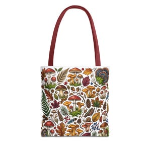 May include: White tote bag with a colorful mushroom and leaf pattern. The bag has a burgundy handle. The design includes various types of mushrooms, acorns, and leaves in shades of red, orange, yellow, and green. A nature-themed accessory.
