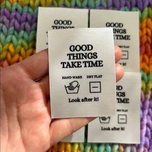 Puede incluir: Etiqueta de tela blanca con texto negro e iconos. El texto dice "Good Things Take Time". Los iconos indican lavado a mano y secado plano. La etiqueta también incluye el texto "Look after it!"