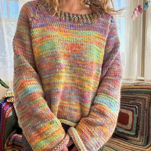 May include: A colourful striped knitted jumper with long sleeves and a round neckline. The jumper is made of a soft, chunky yarn and has a relaxed fit.